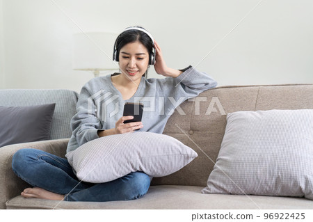 Asian woman listen music with mobile phone and headphones. Calm home weekend, relax while sit on sofa, enjoy favorite tune, popular music, use modern wireless headphones and gadgets in living room 96922425