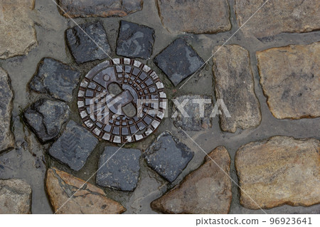 Old metal sewer hatch in the middle of the road, laid out of a smooth paving stone Old metal sewer hatch in the middle of the road, laid out of a smooth paving stone 96923641