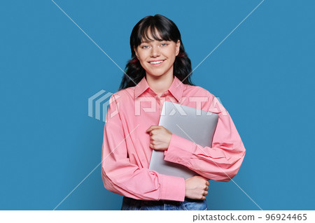 Teenage female student with laptop, looking at camera on blue background Teenage female student with laptop, looking at camera on blue background 96924465