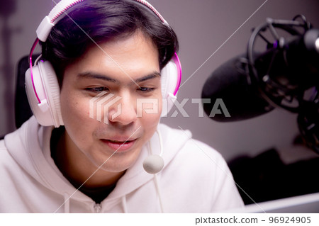 Young asian man for a podcast wearing headphones and speaking with mic in studio. 96924905