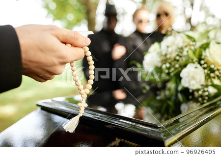 Man holding rosary and praying at outdoor funeral 96926405