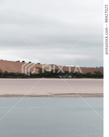 Sandy seashore. Calm water. The remains of an old ship on the shore. A plowed field. Minimalistic landscape. 96927025