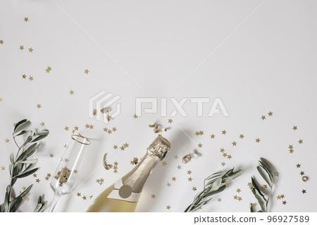 New Year festive web banner. Birthday, wedding party. Celebration concept. Champagne wine bottle, drinking glass. Olive tree branches. White table background. Golden star confetti. Flat lay, top view. 96927589