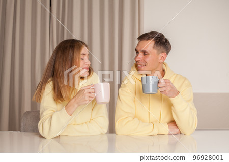 Lovely couple drinking something from the cups and sitting by the table Lovely couple drinking something from the cups and sitting by the table 96928001