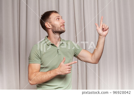 Confident adult man in green t-shirt pointing up against beige background 96928042