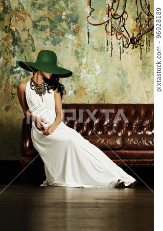 Elegant brunette woman posing in green wide broad brim hat on sofa 96928189