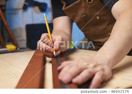 A carpenter making a mark with pencil after measuring a wooden board 96931574