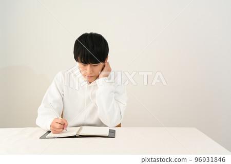 Young man filling out a personal organizer with a pen at his desk Young man filling out a personal organizer with a pen at his desk 96931846