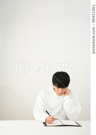 Young man filling out a personal organizer with a pen at his desk Young man filling out a personal organizer with a pen at his desk 96931861