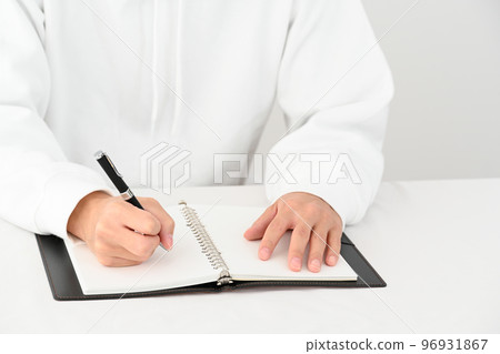 The hand of a young man filling in a system notebook with a pen at a desk 96931867