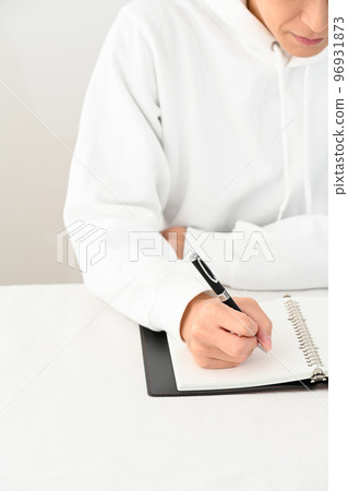 Young man filling out a personal organizer with a pen at his desk Young man filling out a personal organizer with a pen at his desk 96931873