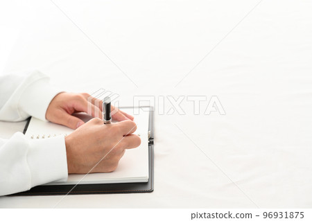 The hand of a young man filling in a system notebook with a pen at a desk 96931875