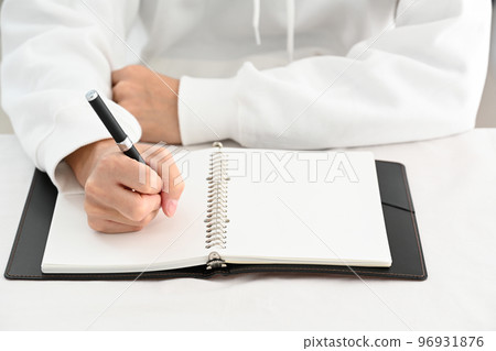 The hand of a young man filling in a system notebook with a pen at a desk 96931876