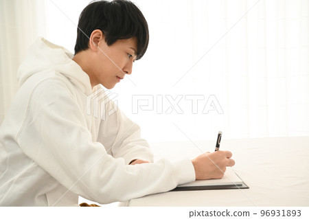 Young man filling out a personal organizer with a pen at his desk 96931893