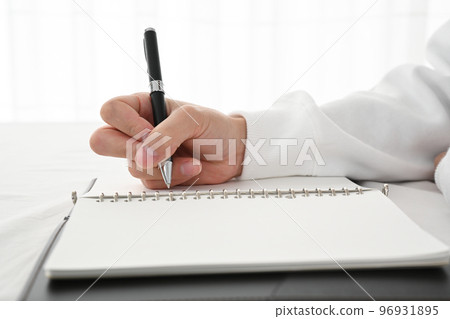 The hand of a young man filling in a system notebook with a pen at a desk 96931895