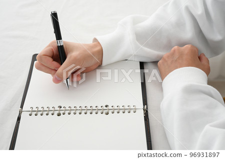 The hand of a young man filling in a system notebook with a pen at a desk 96931897