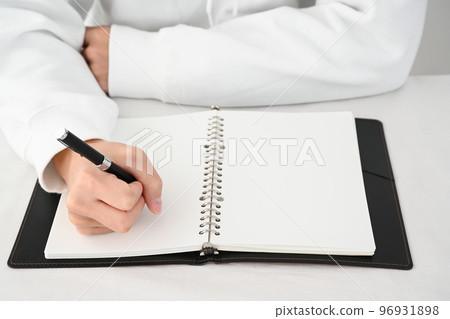 一個年輕人的手在桌上用筆填寫系統筆記本 96931898
