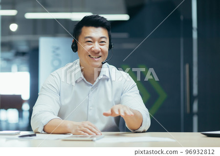 Online business training. Young smiling Asian man sit and talk in the office in front of the camera in a headset, conducts an online meeting, webinar 96932812