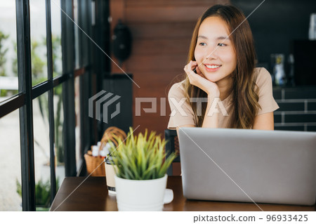 Happy charming woman working outside and smiling in coffee shop freelancer thinking about new ideas, Asian young businesswoman sitting alone at cafe desk with laptop computer she looking out of window Happy charming woman working outside and smiling in coffee shop freelancer thinking about new ideas, Asian young businesswoman sitting alone at cafe desk with laptop computer she looking out of window 96933425