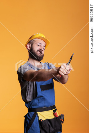 Building contractor using pair of pliers to repair, working as carpenter or constructor in studio. Professional construction worker with hardhat holding pliers and renovating tools on background. 96935917