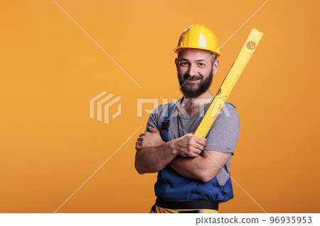 Repairing constructor holding water level ruler in studio, standing with arms crossed. Young repairman preparing to do measurements using professional leveler tool, confident carpenter. 96935953