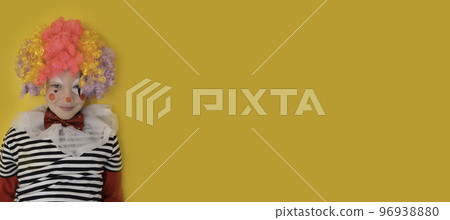 A boy in a clown costume on the background of a bright yellow wall is fooling around and smiling 96938880