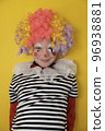 A boy in a clown costume on the background of a bright yellow wall is fooling around and smiling 96938881
