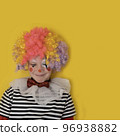 A boy in a clown costume on the background of a bright yellow wall is fooling around and smiling 96938882