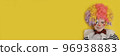 A boy in a clown costume on the background of a bright yellow wall is fooling around and smiling 96938883