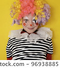 A boy in a clown costume on the background of a bright yellow wall is fooling around and smiling 96938885