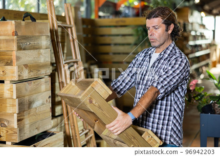 Man choosing wooden box for growing houseplants in gardening store Man choosing wooden box for growing houseplants in gardening store 96942203