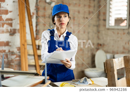 Female worker filling documentation while standing in apartment during repair works 96942286