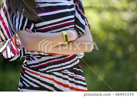 Young woman arms with fitness bracelet on outdoors blurred background. Young woman arms with fitness bracelet on outdoors blurred background. 96943334