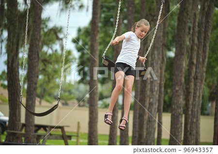 Young pretty excited teenage girl jumping out of the swings on summer vacations sunny day. Danger of accident concept 96943357