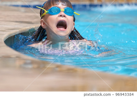 Young child girl in goggles learning to swim in blue pool water outdoors. Summer recreation activity concept Young child girl in goggles learning to swim in blue pool water outdoors. Summer recreation activity concept 96943384