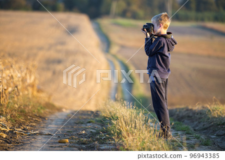 Young child boy with photo camera taking picture of wheat field on blurred rural background. Young child boy with photo camera taking picture of wheat field on blurred rural background. 96943385