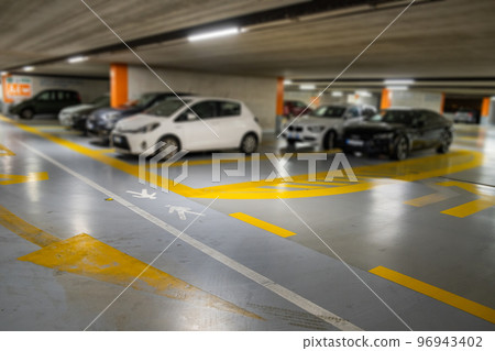Yellow markings with blurred modern cars parked inside closed underground parking lot. Yellow markings with blurred modern cars parked inside closed underground parking lot. 96943402