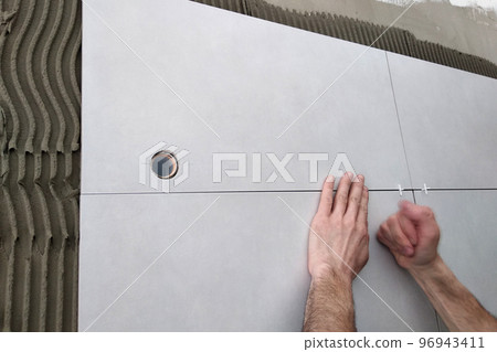 Worker hands putting ceramic tiles on the wall. Worker hands putting ceramic tiles on the wall. 96943411