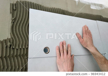 Worker hands putting ceramic tiles on the wall. Worker hands putting ceramic tiles on the wall. 96943412