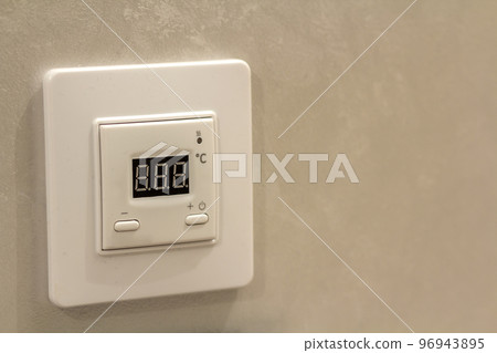 White electronic programmable digital thermostat on light wall copy space background. Climate control, comfortable home temperature, energy saving concept. 96943895