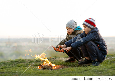 Two children playing with fire outdoors in cold weather. 96944039