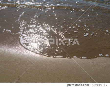 沙灘的溫柔海浪反射著陽光，閃閃發光。 96944117