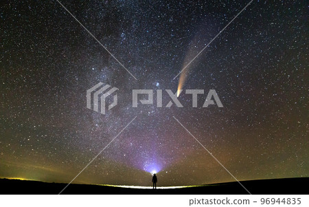 Small silhouette of a scientist with flashlight on his head pointing bright beam of light on starry sky with C/2020 F3 (NEOWISE) comet with light tail. Space exploration concept. 96944835