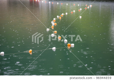 Rope with white and yellow restriction markers on water surface for prohibiting of swimming in deep lake or sea. Rope with white and yellow restriction markers on water surface for prohibiting of swimming in deep lake or sea. 96944859