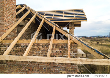 Private residential house with wooden roof frame structure under construction. Unfinished brick building under development. 96944884