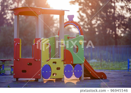 Nursery playground with colorful slides on soft rubber flooring with no children at sunset or sunrise. 96945546