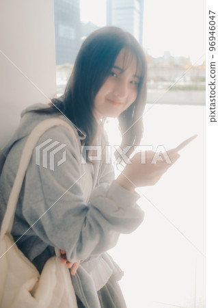 A picture of a high school girl holding a smartphone in the city 96946047