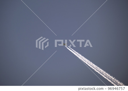 Distant passenger jet plane flying on high altitude on clear blue sky leaving white smoke trace of contrail behind. Air transportation concept 96946757
