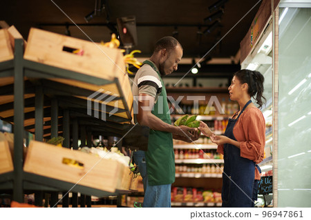Supermarket workers in aprons discussing where to put fresh fruits Supermarket workers in aprons discussing where to put fresh fruits 96947861