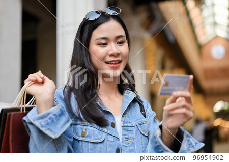 Beautiful Asian female holding a credit card, carrying shopping bags, enjoys shopping at the mall. 96954902